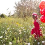 Foto: Frau mit rotem Kleid und Luftballons läuft durch eine Blumenwiese