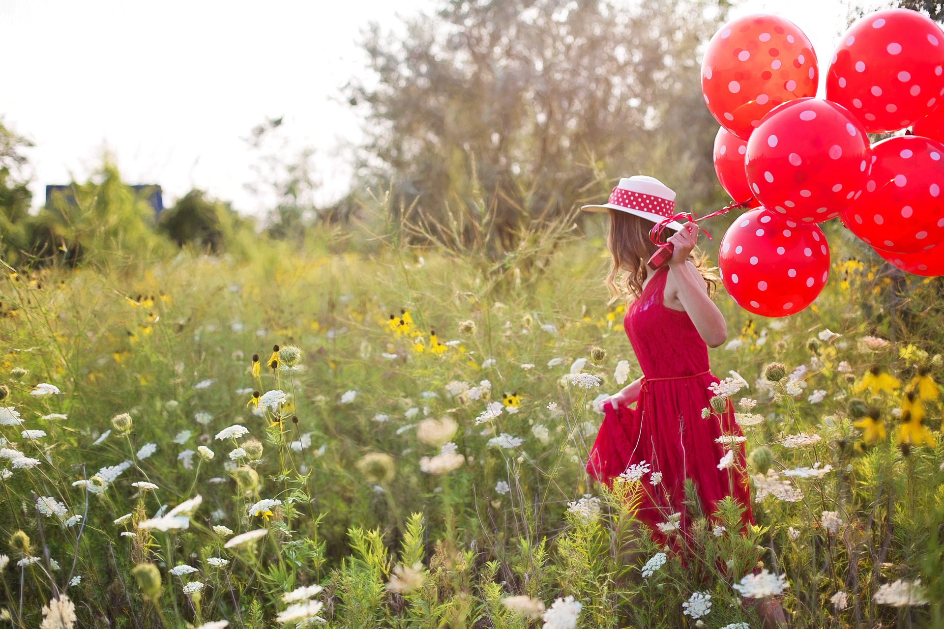 Foto: Frau mit rotem Kleid und Luftballons läuft durch eine Blumenwiese