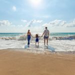 Foto: Familie am Meer, Kind hält Vater und Mutter an den Händen, Rückenansicht