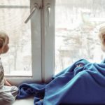 Foto: Mädchen und Kleinkind sitzen vor einem Fenster und blicken nach draußen