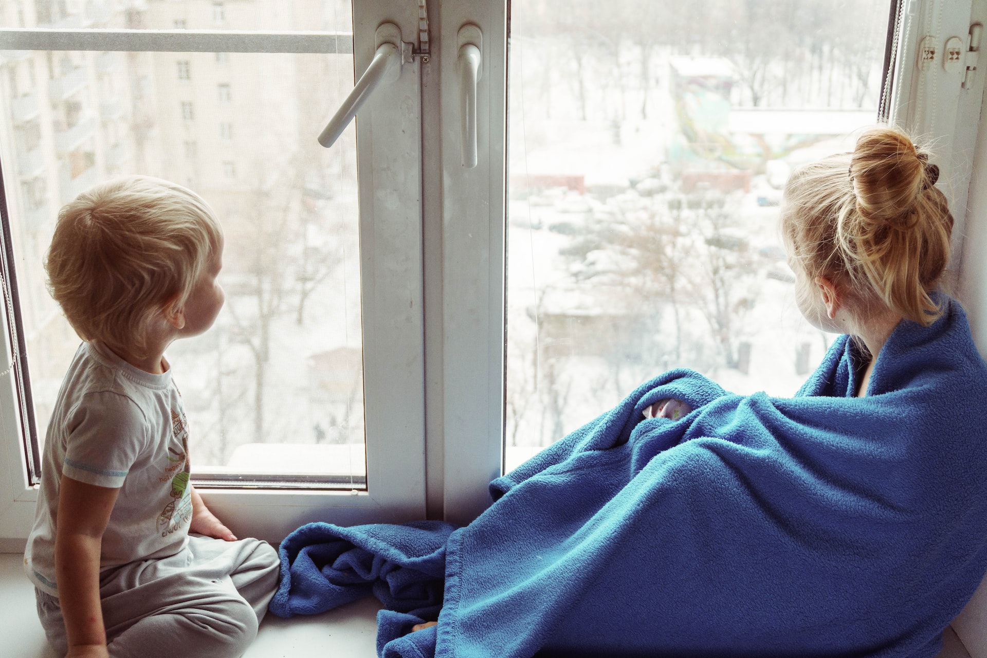 Foto: Mädchen und Kleinkind sitzen vor einem Fenster und blicken nach draußen