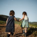 Foto: Zwei kleine Mädchen von hinten halten sich an der Hand und laufen einen Weg entlang